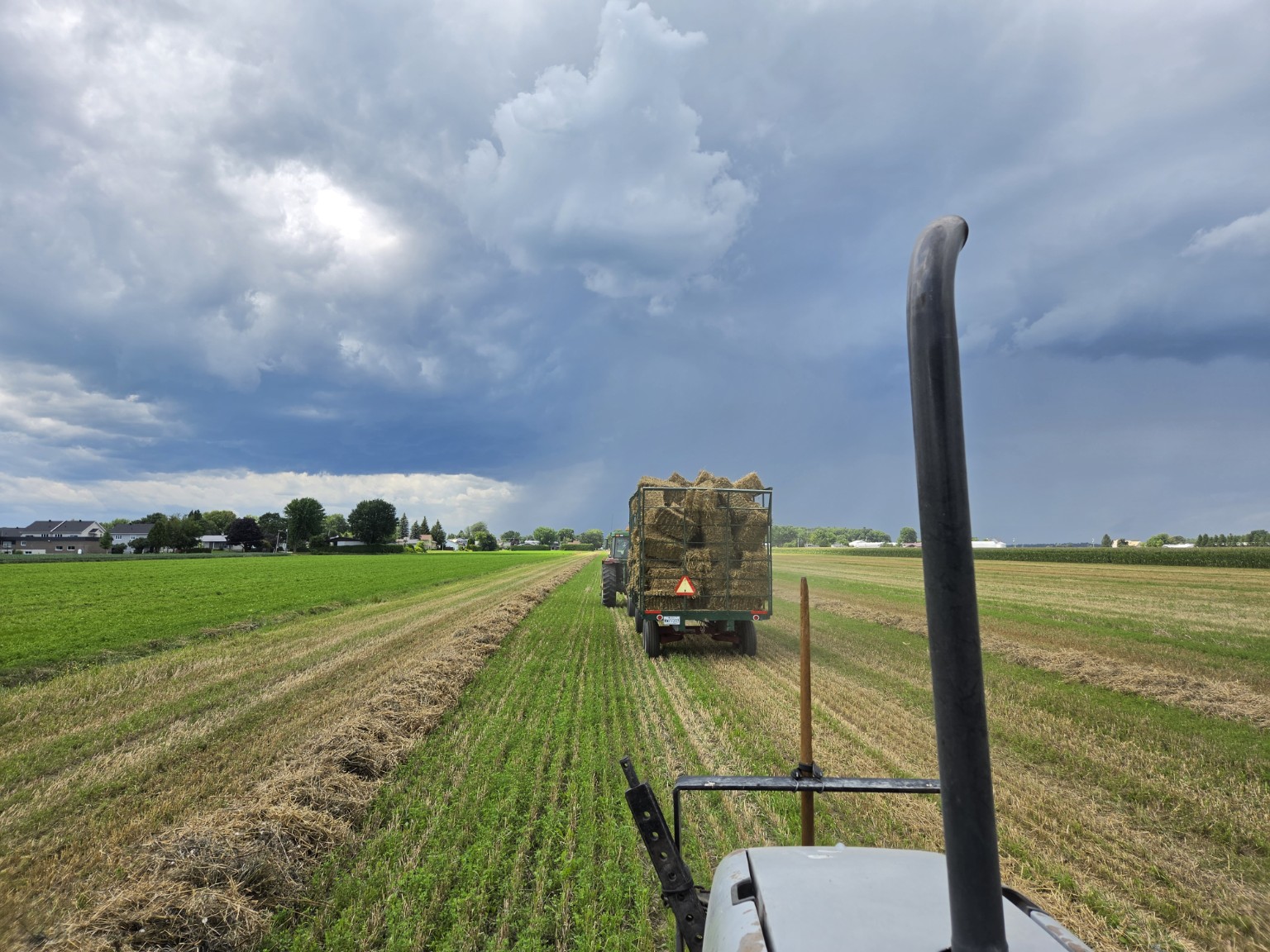 Un wagon chargé de petites balles de paille d’orge avance sous un ciel d’orage.